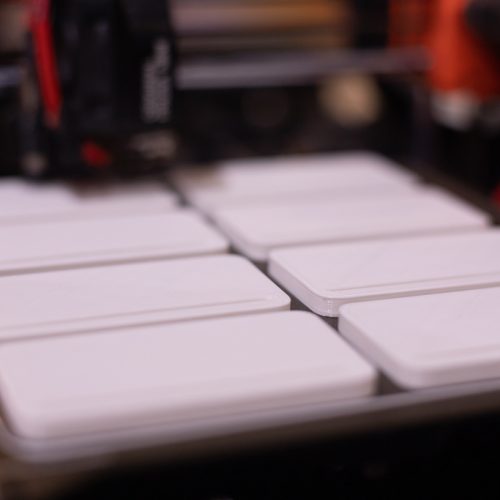 weiße viereckige Rechtecke werden von einem schwarz-orangenen 3D-Drucker gedruckt.