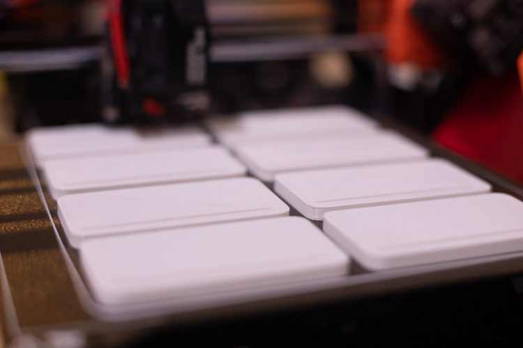 weiße viereckige Rechtecke werden von einem schwarz-orangenen 3D-Drucker gedruckt.