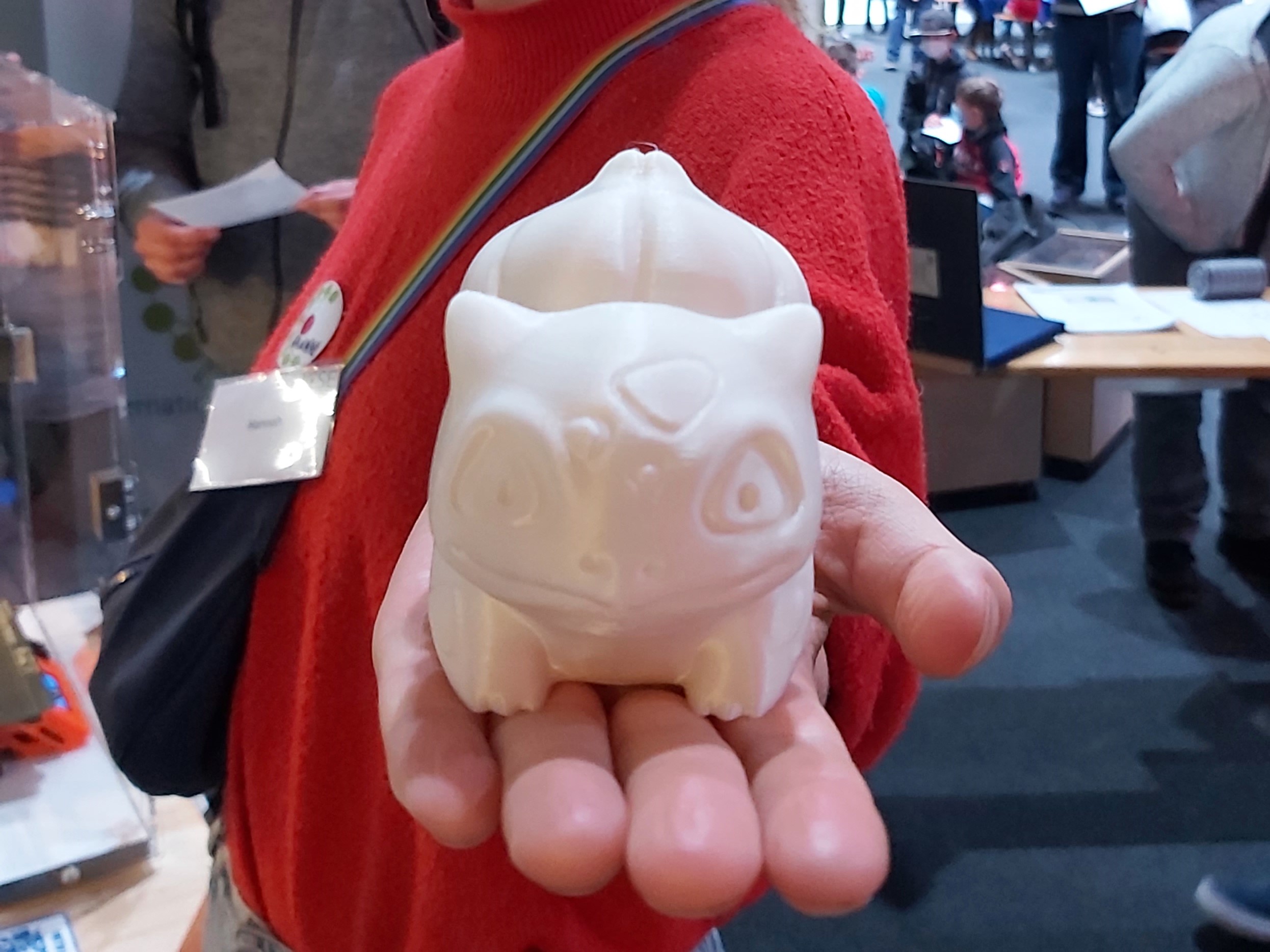 3D gedruckter weißer Bisasam wird von einer weißen Person in rotem Pullover auf der Hand in die Kamer präsentiert.