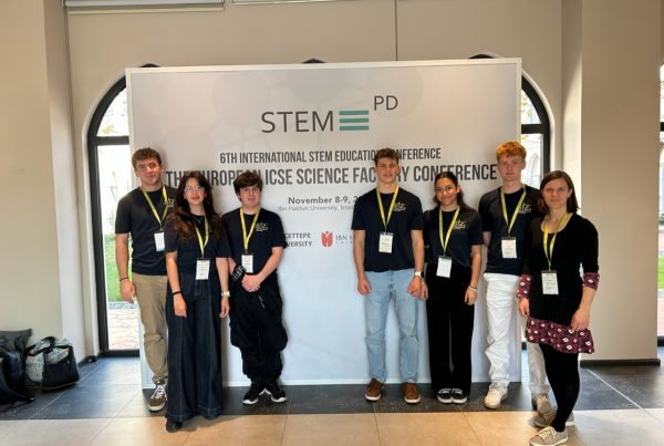 6 Schüler*innen und eine Lehrerin stehen in schwarzen T-Shirts vor einem Banner auf dem steht STEM PD.