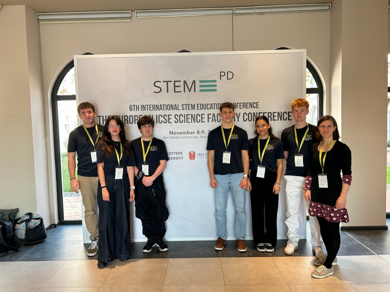 6 Schüler*innen und eine Lehrerin stehen in schwarzen T-Shirts vor einem Banner auf dem steht STEM PD.